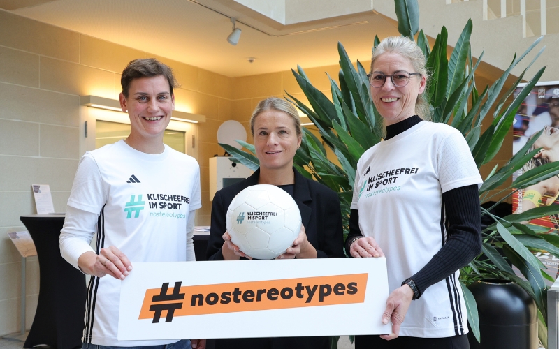 Juliana Groß, Verena Bentele und Romy Stühmeier halten einen #nostereotypes-Banner und einen Klischeefrei im Sport-Ball