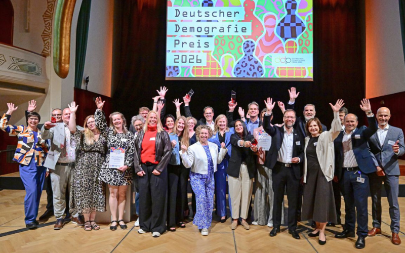 Die Gruppe bei der Preisverleihung steht auf der Bühne und winkt in die Kamera