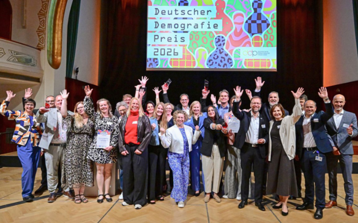 Die Gruppe bei der Preisverleihung steht auf der Bühne und winkt in die Kamera