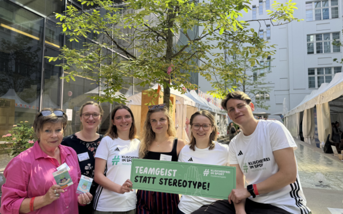 Das kompetenzz-Team steht im Innenhof und hält ein Schild mit der Aufschrift Teamgeist statt Stereotype hoch.