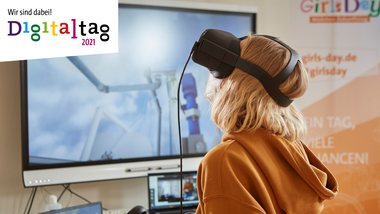 Ein Mädchen trägt eine VR-Brille und schaut nach oben. Oben links ist das Logo vom Digitaltag 2021 mit dem Schriftzug "Wir sind dabei" zu sehen.
