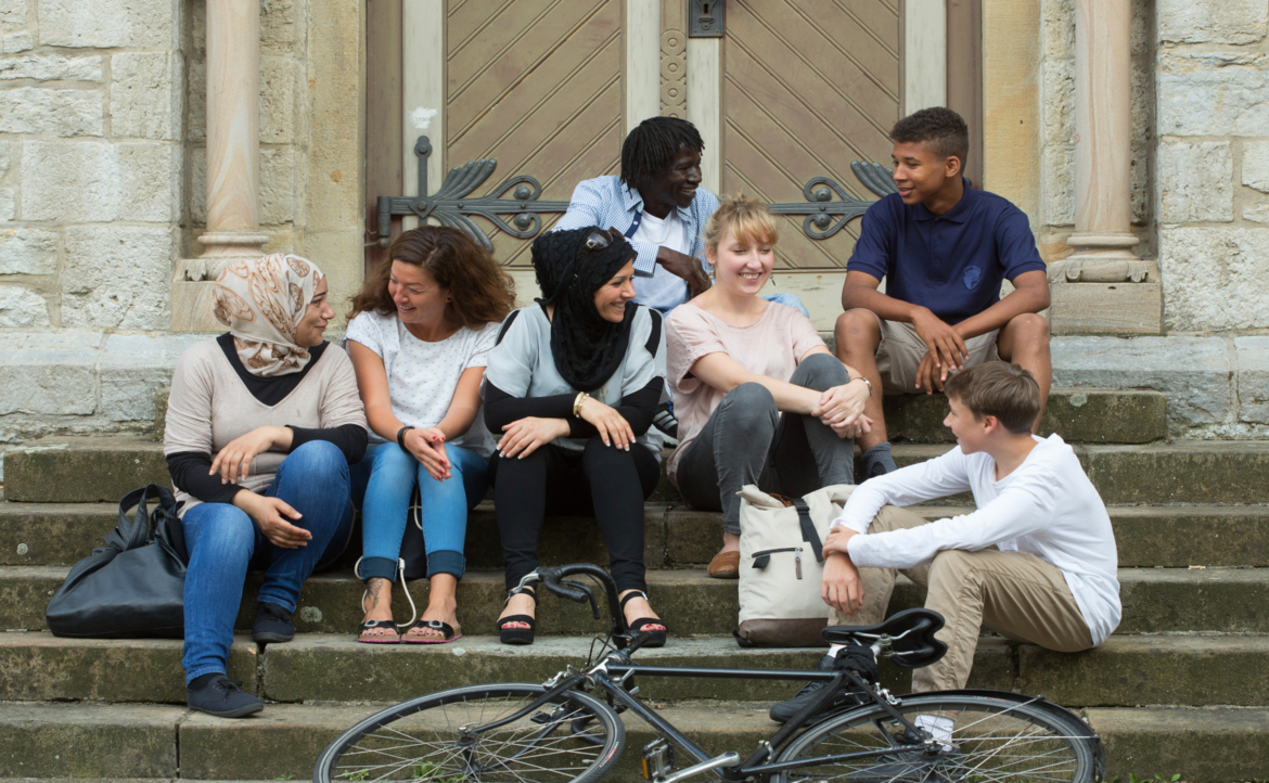 DWK-Integration-Gruppe Eine Gruppe Menschen unterschiedlichen Aussehens sitzt auf einer Treppe